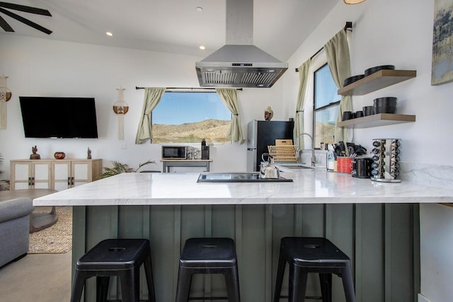 kitchen featuring island exhaust hood, a breakfast bar area, kitchen peninsula, and light stone countertops