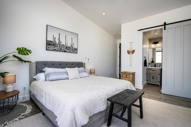 bedroom featuring hardwood / wood-style flooring, connected bathroom, lofted ceiling, and a barn door