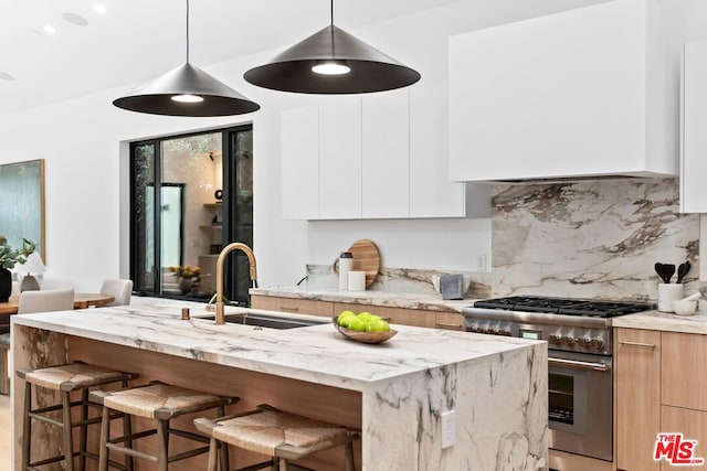 kitchen with white cabinetry, an island with sink, sink, high end range, and light stone counters