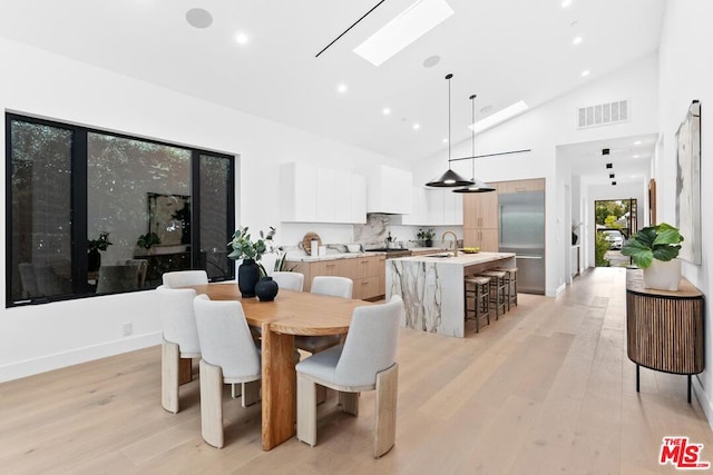 dining area with sink, light hardwood / wood-style flooring, high vaulted ceiling, and a skylight