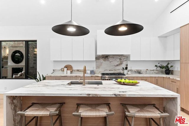 kitchen with sink, white cabinetry, hanging light fixtures, a kitchen island with sink, and stove