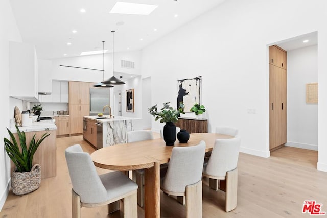 dining space featuring high vaulted ceiling, sink, light wood-type flooring, and a skylight