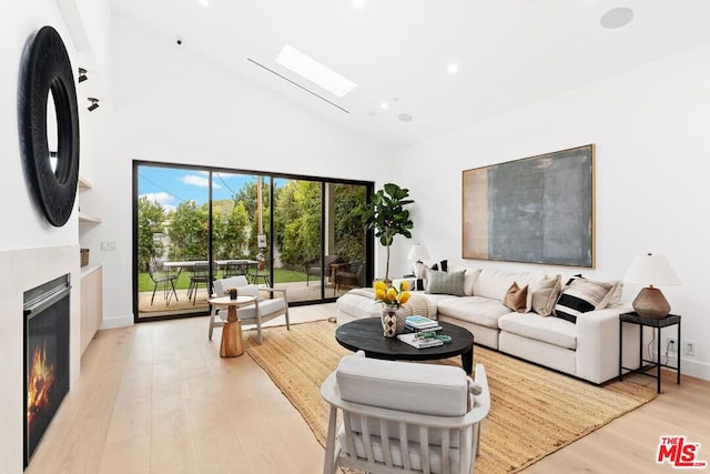 living room with a skylight, high vaulted ceiling, and light hardwood / wood-style flooring