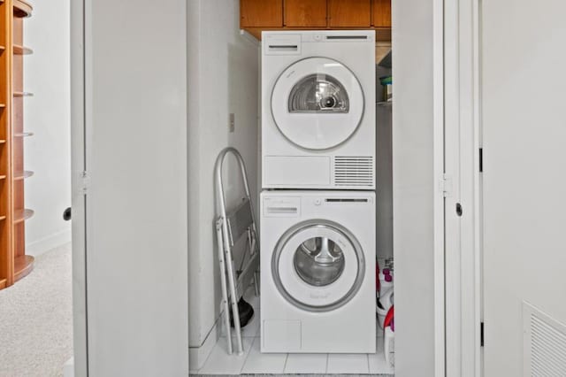 clothes washing area featuring stacked washer and dryer and cabinets