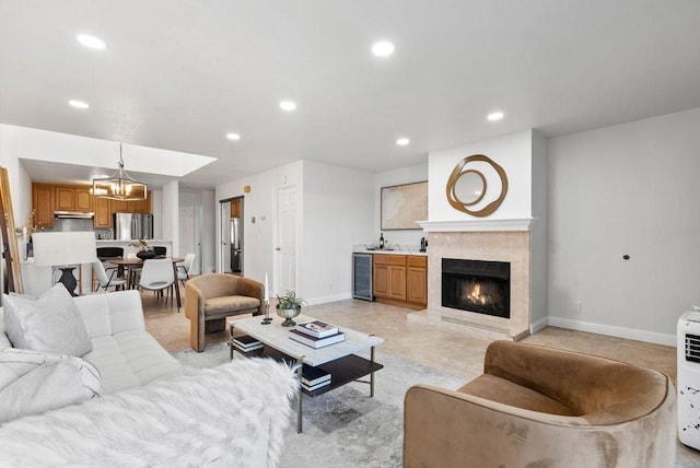 living room featuring wine cooler, a tile fireplace, sink, an inviting chandelier, and light tile patterned floors