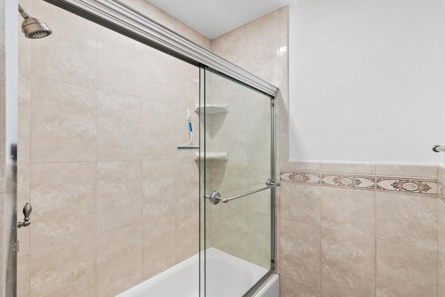 bathroom with tile walls and shower / bath combination with glass door