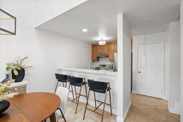 kitchen featuring decorative backsplash, sink, appliances with stainless steel finishes, a breakfast bar area, and light tile patterned floors