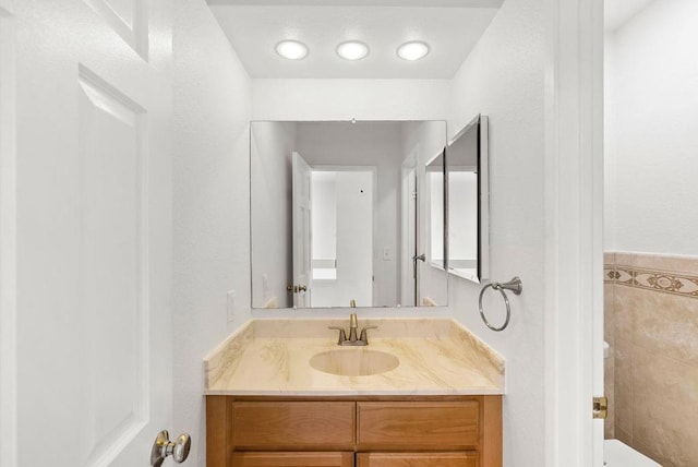 bathroom featuring toilet, vanity, and tile walls