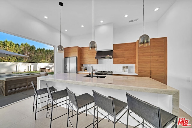 kitchen with stainless steel fridge, decorative backsplash, a spacious island, wall chimney exhaust hood, and sink