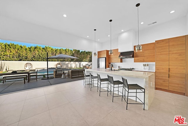 kitchen featuring a breakfast bar area, appliances with stainless steel finishes, a spacious island, decorative light fixtures, and wall chimney exhaust hood