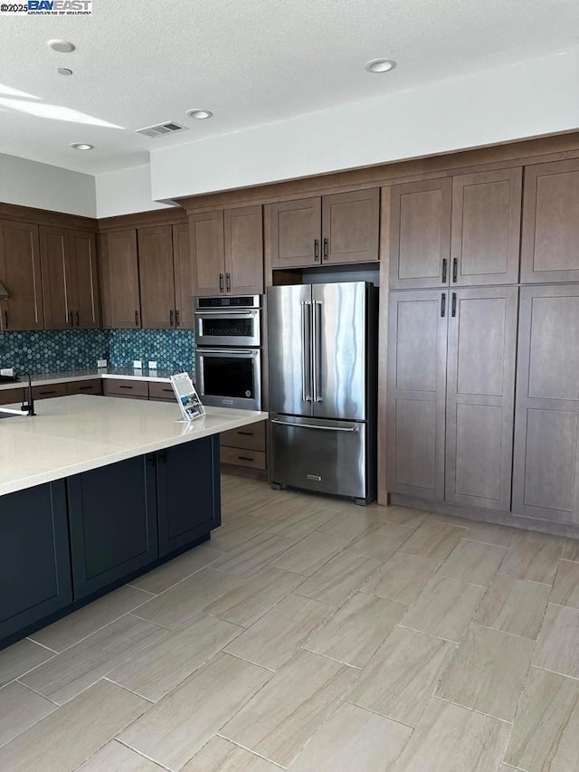 kitchen featuring stainless steel appliances, decorative backsplash, a textured ceiling, dark brown cabinetry, and sink