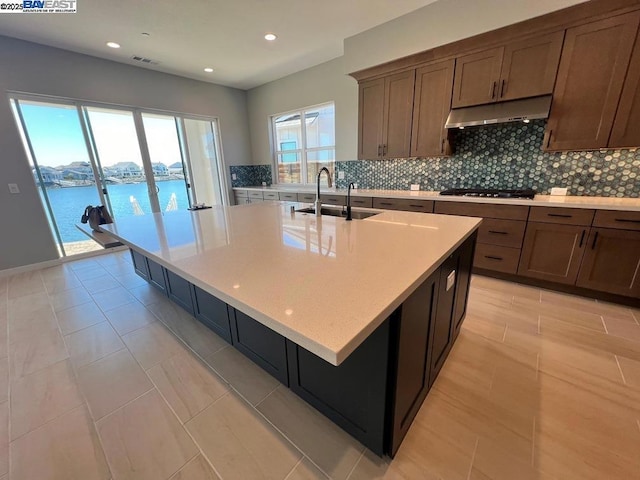 kitchen featuring light tile patterned floors, an island with sink, black gas cooktop, a water view, and sink