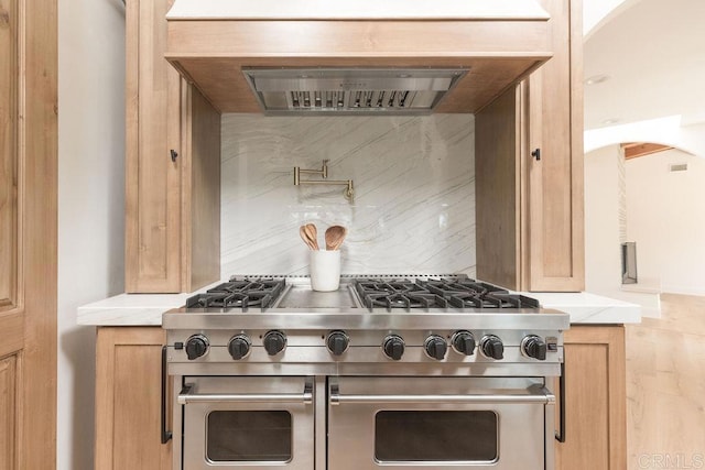 kitchen featuring decorative backsplash, range with two ovens, and wall chimney range hood