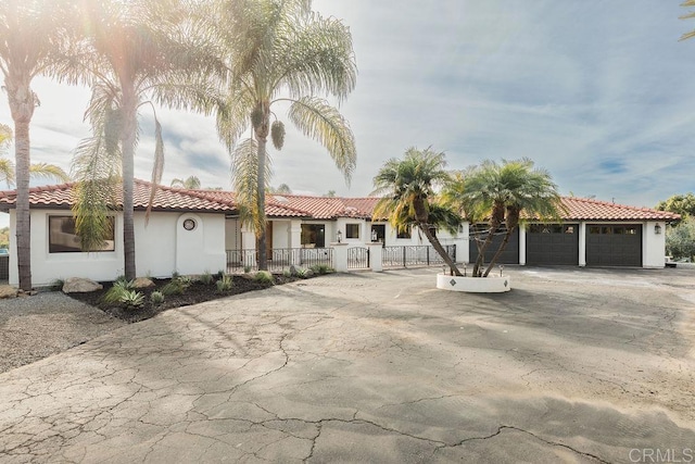mediterranean / spanish home featuring fence, stucco siding, an attached garage, driveway, and a tile roof