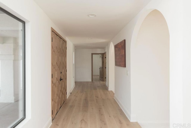 hall featuring arched walkways, baseboards, and light wood-type flooring