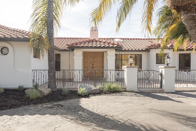 mediterranean / spanish-style house featuring a tiled roof, a gate, fence private yard, and stucco siding