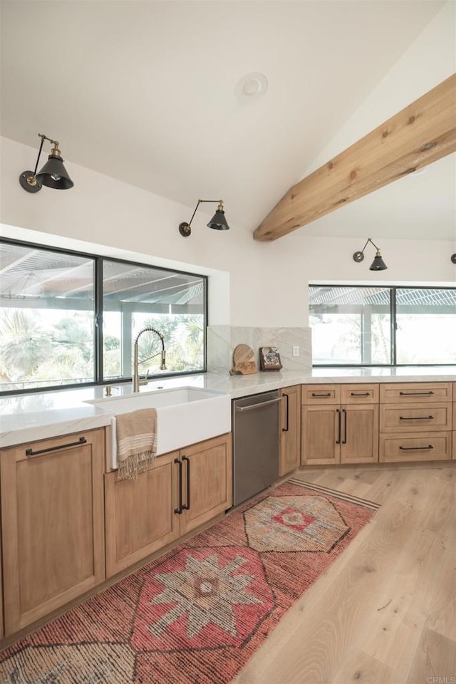 kitchen with stainless steel dishwasher, light countertops, a sink, light wood-style flooring, and vaulted ceiling