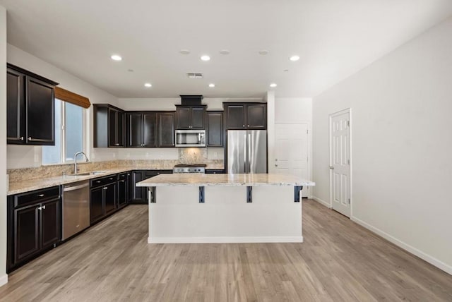 kitchen featuring sink, light stone countertops, a kitchen bar, a center island, and stainless steel appliances