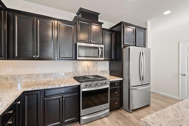 kitchen featuring light stone counters, tasteful backsplash, light hardwood / wood-style flooring, and appliances with stainless steel finishes