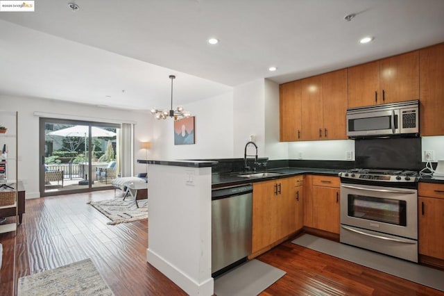 kitchen featuring kitchen peninsula, stainless steel appliances, dark hardwood / wood-style floors, a notable chandelier, and sink