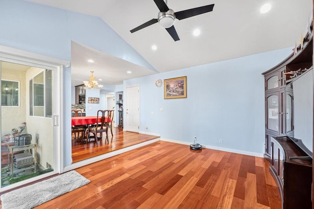 living room with wood-type flooring, ceiling fan with notable chandelier, and high vaulted ceiling