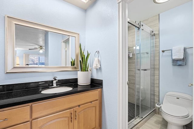 bathroom with walk in shower, ceiling fan, vanity, and toilet