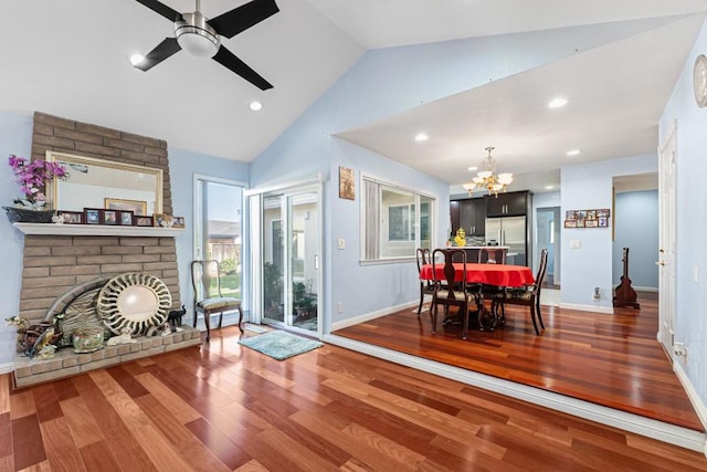 dining room featuring hardwood / wood-style flooring, a brick fireplace, ceiling fan with notable chandelier, and high vaulted ceiling