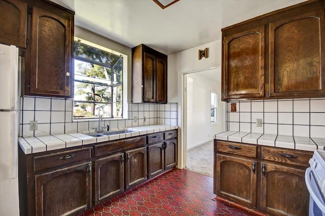 kitchen featuring white fridge, sink, backsplash, tile countertops, and dark brown cabinets