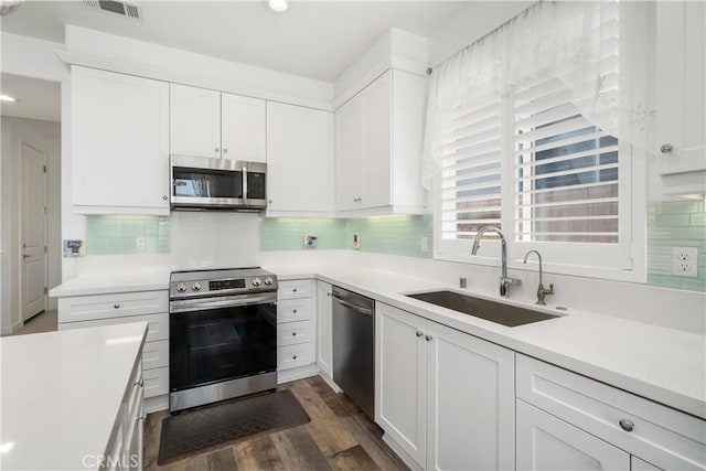 kitchen featuring stainless steel appliances, backsplash, dark wood-type flooring, white cabinets, and sink