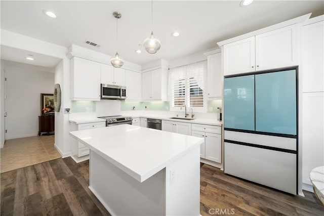 kitchen with white cabinets, dark wood-type flooring, stainless steel appliances, sink, and hanging light fixtures