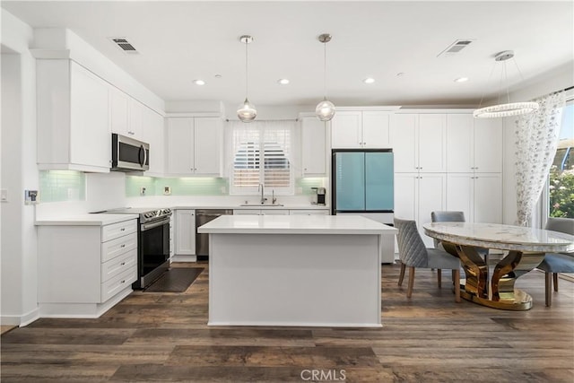 kitchen with appliances with stainless steel finishes, dark hardwood / wood-style floors, pendant lighting, white cabinets, and sink