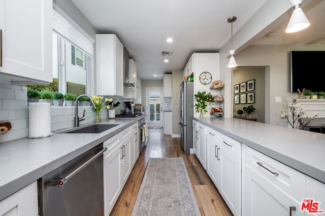 kitchen featuring appliances with stainless steel finishes, sink, white cabinets, and decorative light fixtures