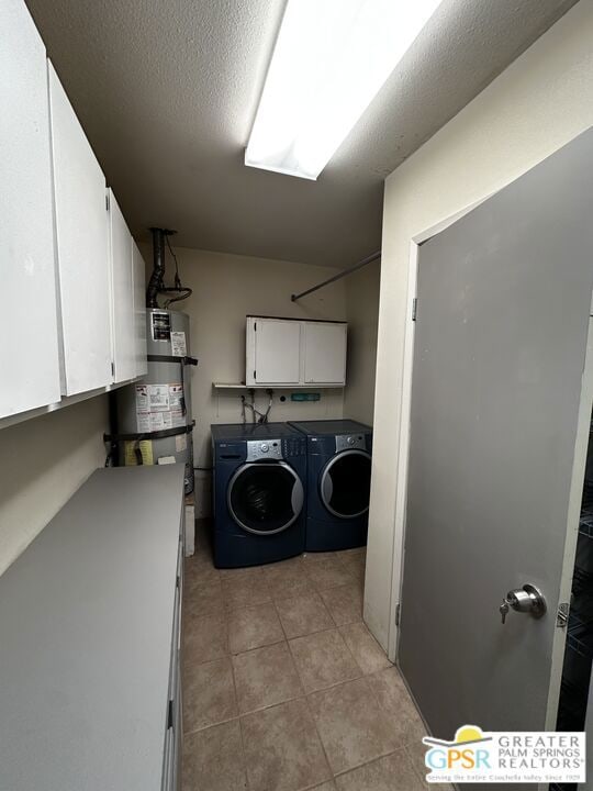 clothes washing area featuring secured water heater, a textured ceiling, washer and dryer, cabinets, and light tile patterned flooring