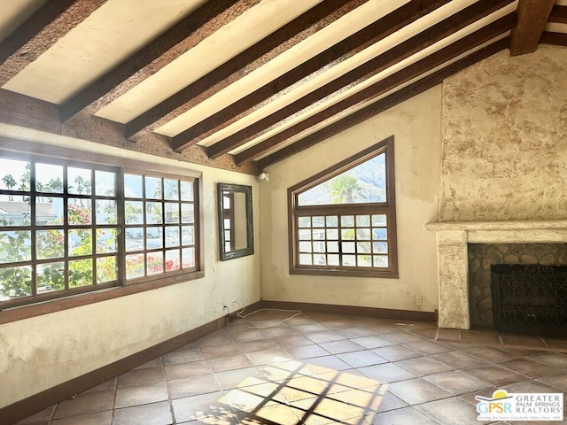 unfurnished living room featuring a healthy amount of sunlight, beamed ceiling, and a stone fireplace