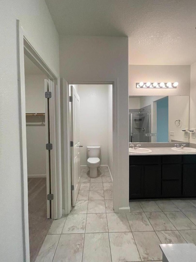 bathroom with a textured ceiling, toilet, vanity, and walk in shower