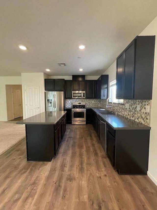 kitchen featuring hardwood / wood-style floors, appliances with stainless steel finishes, a kitchen island, decorative backsplash, and sink