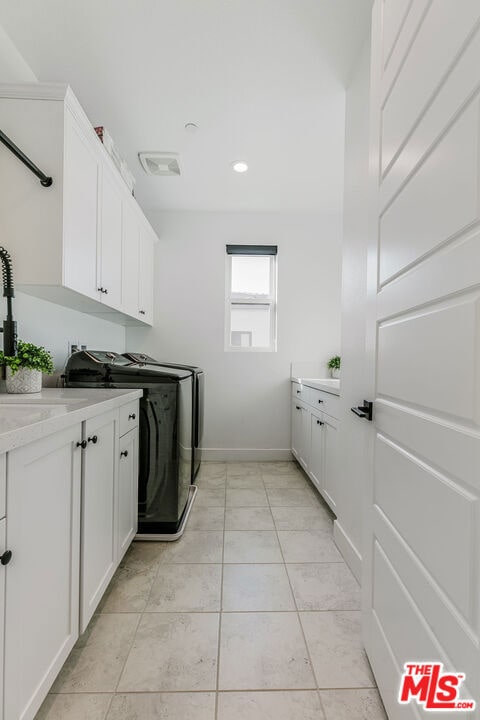 clothes washing area with cabinets, light tile patterned floors, washer and clothes dryer, and sink