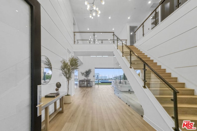 stairway with hardwood / wood-style floors, a towering ceiling, and a notable chandelier