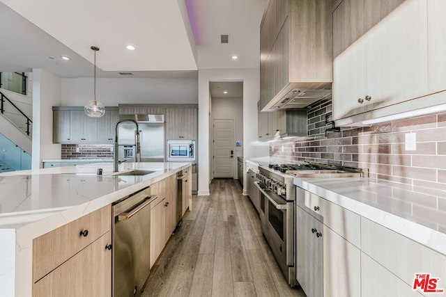 kitchen featuring decorative light fixtures, sink, built in appliances, light brown cabinets, and custom range hood