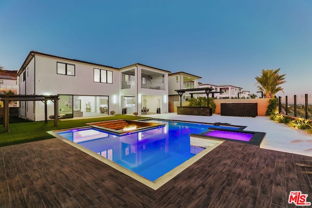 pool at dusk with an in ground hot tub and a pergola