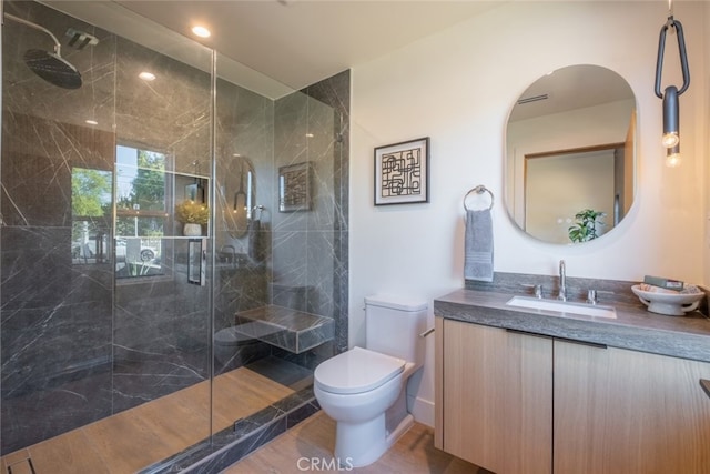 bathroom featuring toilet, vanity, a tile shower, and hardwood / wood-style floors