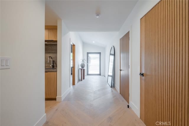 hall with vaulted ceiling, sink, and light parquet floors