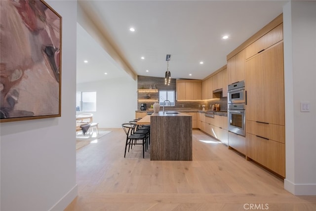 kitchen with pendant lighting, light brown cabinetry, sink, a kitchen breakfast bar, and a kitchen island with sink