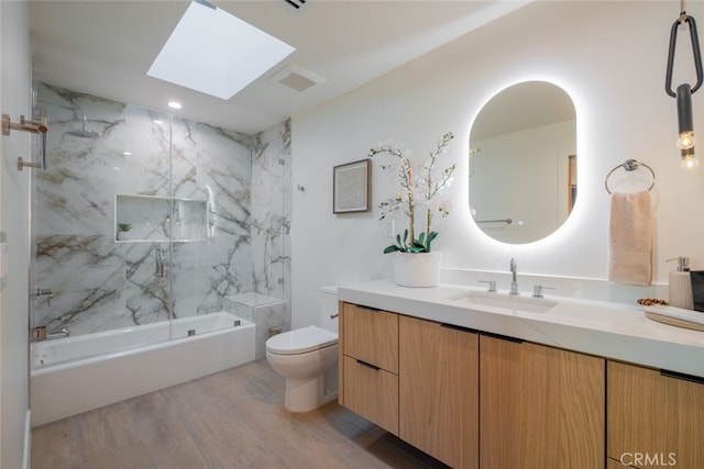 full bathroom featuring tiled shower / bath combo, wood-type flooring, vanity, a skylight, and toilet