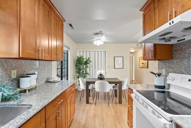 kitchen with tasteful backsplash, light stone countertops, white electric range oven, and light wood-type flooring