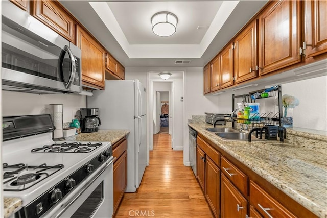 kitchen with light hardwood / wood-style floors, appliances with stainless steel finishes, a raised ceiling, light stone counters, and sink