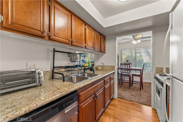 kitchen featuring light stone countertops, white appliances, sink, ceiling fan, and light hardwood / wood-style flooring