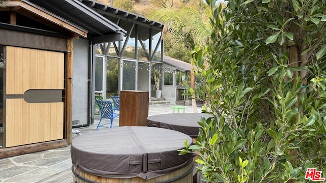 view of patio / terrace featuring glass enclosure and a hot tub