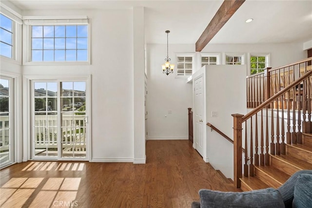 foyer entrance featuring hardwood / wood-style flooring, a wealth of natural light, beam ceiling, and a notable chandelier