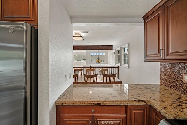 kitchen with backsplash, light stone counters, and stainless steel refrigerator